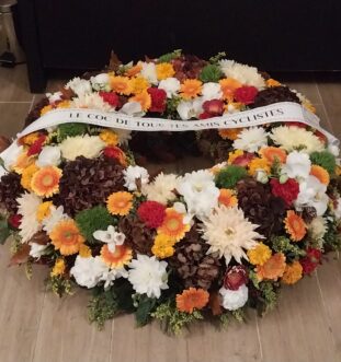 Grosse couronne funéraire multicolore avec hortensias bordeaux, chrysanthèmes blancs, œillets de poète verts, germinis jaunes, oeillets orangés, solidago et feuilles de chêne